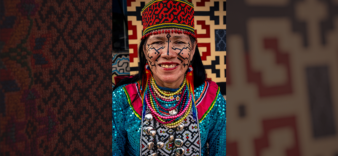 Woman wearing traditional beaded hat, colorful sequined fabric, and layered necklaces with metal ornaments