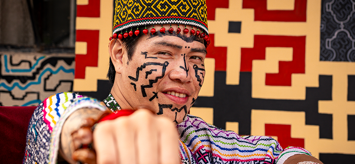 Man with traditional face paint wearing woven fabric clothing and a patterned textile hat in red, yellow, and black