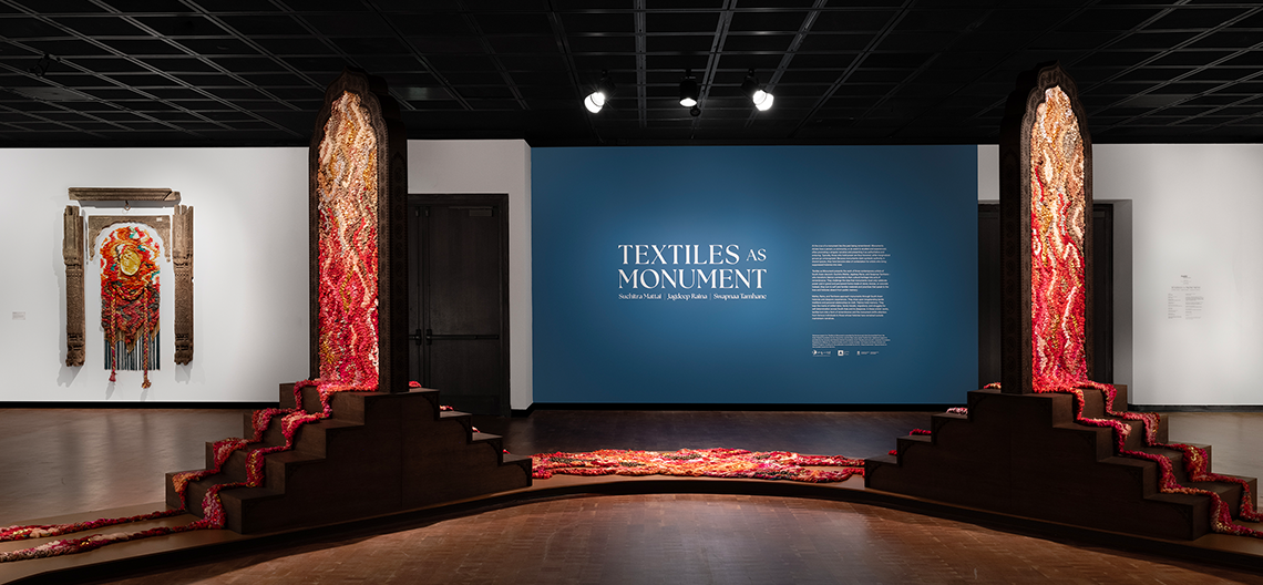 Textile art installation with fabric and yarn in red and orange hues displayed on wooden frames in gallery